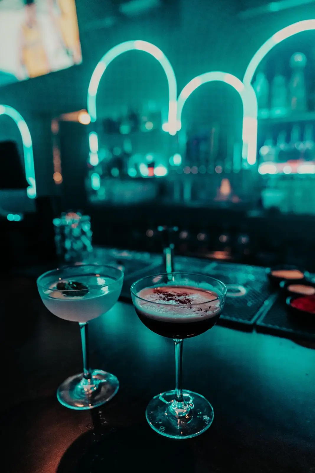 Two martinis on the teal-lit bar