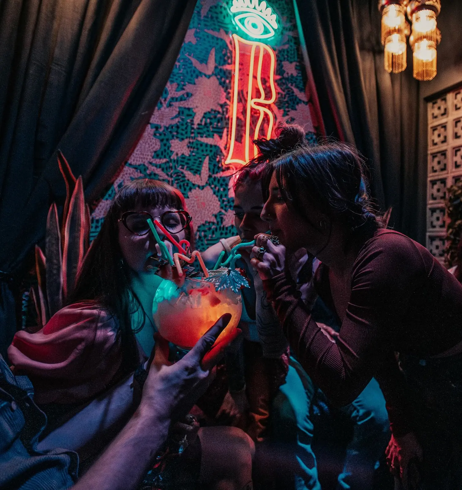 Two friends sipping cocktails under a neon Bazaar B sign